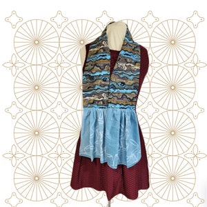 May include: A blue and brown patterned scarf with a blue and white apron. The apron has a ruffled bottom and a white design.