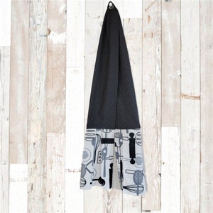 May include: A black and white kitchen towel with a pattern of kitchen utensils. The towel is hanging on a hook. The towel is made of a soft, absorbent material.