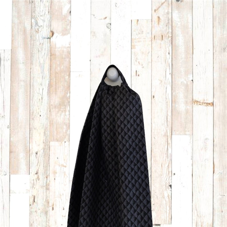 May include: Black fabric with a diamond pattern, hanging against a white wooden backdrop.