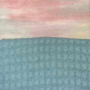 May include: A close-up of a blue textured fabric with a pink and white watercolour-like design on top.