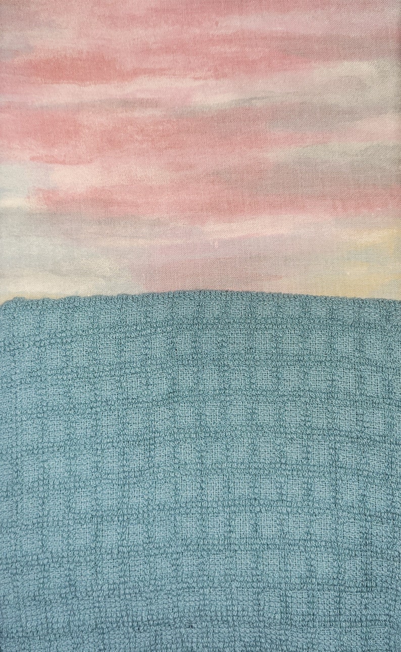 May include: A close-up of a blue textured fabric with a pink and white watercolour-like design on top.