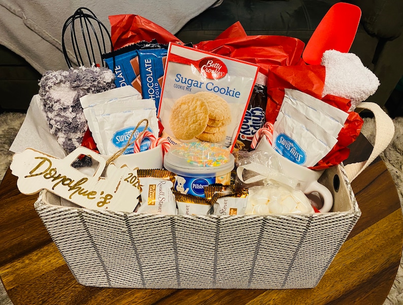 May include: A gift basket filled with baking supplies, including cookie mix, chocolate bars, Swiss Miss packets, and a mug. The basket has a black and white woven pattern and a wooden tag that says "Donahue's 2023".
