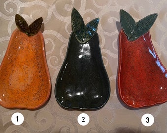 May include: Three ceramic pear-shaped serving dishes with green leaf accents. The dishes are orange, black, and red.
