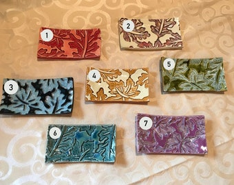 May include: Seven small rectangular ceramic dishes with a leaf design. The dishes are in various colors, including blue, green, purple, orange, and white.