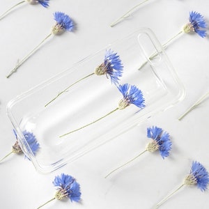 May include: A clear phone case with two pressed blue flowers inside. The flowers are arranged vertically in the case.