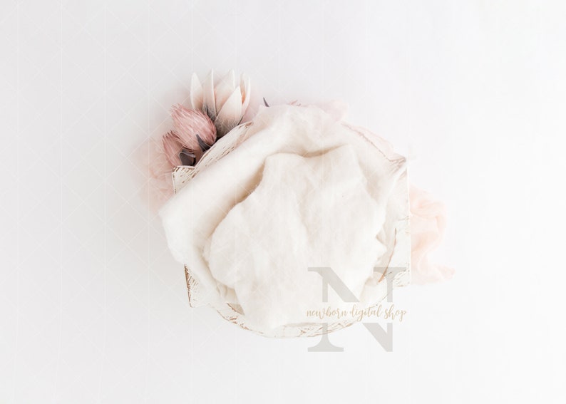 May include: A newborn photography prop arrangement featuring a white wooden bowl with a soft, cream-colored blanket and delicate pink flowers. The scene is set against a white backdrop, creating a serene and gentle aesthetic.