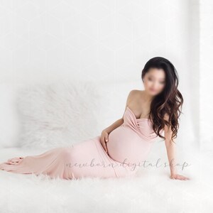 May include: A pregnant person wearing a pink strapless maternity gown, sitting on a white fluffy surface. The person has long dark hair and is looking down at their stomach.