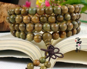 May include: A wooden beaded bracelet with a brown tassel. The beads are a light green and brown color and are arranged in a circular pattern. The bracelet is lying on a book.