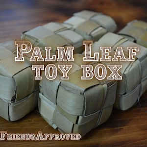 May include: Five woven palm leaf toy boxes on a wooden surface. The boxes are light brown and have a woven pattern. The text "PALM LEAF TOY BOX" is written in brown letters on a wooden background.