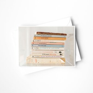 May include: A stack of vintage books with colorful spines, including titles by C.S. Lewis. The books are arranged on a white background, with a white envelope partially visible. The books have titles like "The Lion, the Witch and the Wardrobe."