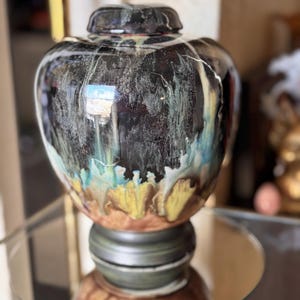 May include: A large, round ceramic vase with a black, blue, and yellow glaze. The vase has a wide mouth and a narrow base. It is decorated with a swirling pattern of colors.