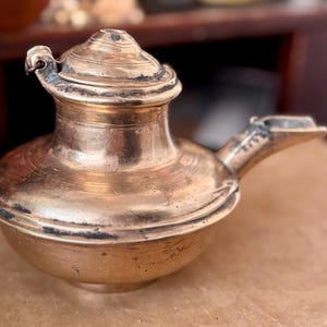 May include: A vintage brass teapot with a lid and a spout. The teapot has a round body and a small handle.