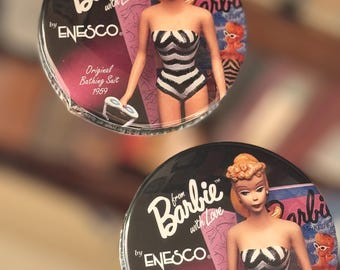 May include: Two round, silver-colored, decorative coasters featuring a black and white striped swimsuit-clad Barbie doll. The text "from Barbie with Love by ENESCO" and "Original Bathing Suit 1959" is printed on each coaster.