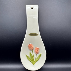 May include: Cream-colored, hand-painted ceramic spoon rest with a tulip design. The spoon rest features two raised, peach-colored tulips with green leaves. The word "Handpainted" is printed on a small oval sticker.