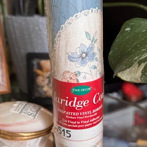 May include: A roll of prepasted vinyl border wallpaper with a floral pattern in shades of blue, pink, and green. The border features a scalloped edge and the text "Fine-Decor Carriage Cottage" and "4515".