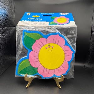 May include: A package of colorful flower-shaped bulletin board accents. The flowers are pink, yellow, and blue, with a smiling face in the center. The package reads "Flowers" and "36 Bulletin Board Accents."