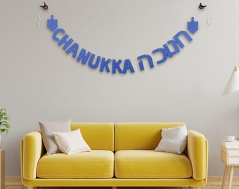 May include: Blue "CHANUKKA" banner with Hebrew text and dreidel shapes, hanging on a wall above a yellow sofa. The banner is a festive decoration for the Jewish holiday of Hanukkah.