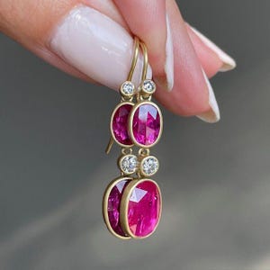 Könnte beinhalten: Ein Paar Ohrhänger mit zwei oval geschliffenen, leuchtend pinken Edelsteinen und zwei rund geschliffenen, klaren weißen Diamanten in Gelbgold gefasst. Das vertikale Design zeigt einen kleinen Diamanten über jedem ovalen Edelstein, befestigt an Goldhaken.