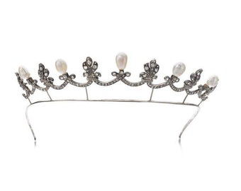 Puede incluir: Una tiara de plata con un diseño delicado que presenta pequeñas perlas blancas y piedras transparentes. La tiara está hecha de metal y tiene una forma curva.