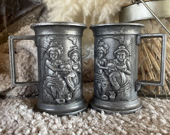 Zestaw kubków z cyny w stylu vintage: klasyczne kufle z reliefem przedstawiającym scenę Bachusa, rustykalna para naczyń barmańskich