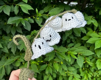 May include: A crocheted lily of the valley flower with white bells and green stems. Each bell has a cute, cartoon-like face.