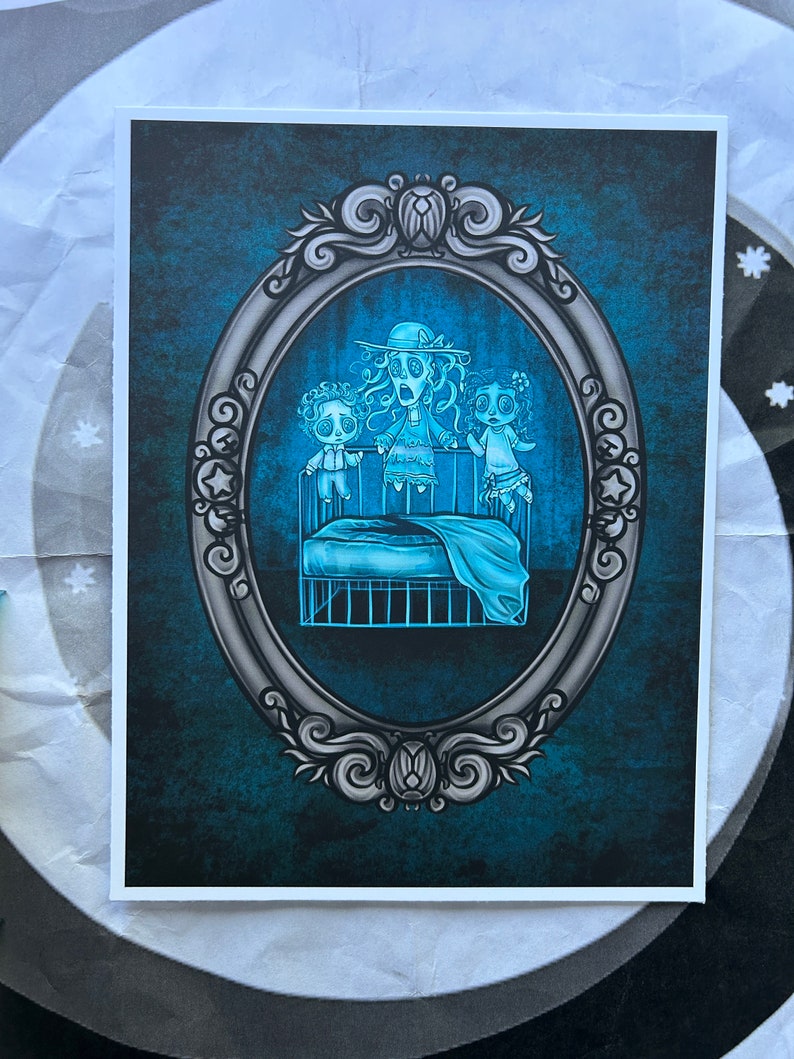 May include: A vintage-style oval frame with a blue and gray background. Inside the frame, three ghostly figures are depicted standing in a crib. The figures are translucent and have large, wide eyes. The crib is made of metal and has a blue blanket.