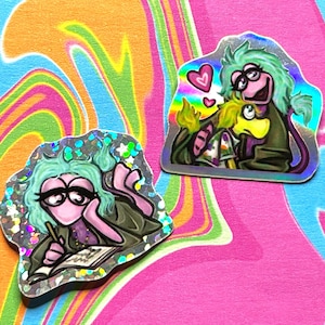 May include: Two holographic stickers featuring a pink and green character with glasses. One sticker shows the character writing in a notebook, the other shows the character hugging a yellow character with a heart above them.