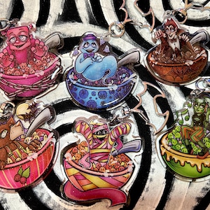 May include: Six colorful keychains featuring cartoon characters in a bowl of cereal. Each keychain has a different character, including a ghost, a mummy, a werewolf, a vampire, a zombie, and a monster. The keychains are made of clear acrylic and have a glossy finish.