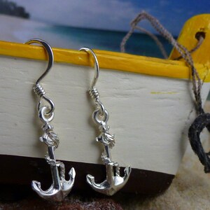 Könnte beinhalten: Ein Paar silberne Ankerohrringe mit einem Seildetail. Die Ohrringe hängen an einer Holzoberfläche.