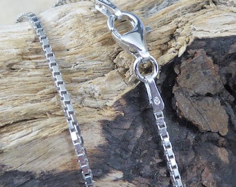 May include: A silver chain necklace with a box clasp. The chain is made of small, square links.