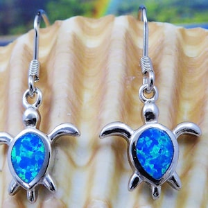 Puede incluir: Un par de pendientes colgantes de plata con un dije de tortuga de ópalo azul. Los pendientes tienen un cierre de gancho simple.
