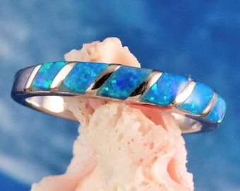 Pode incluir: Um anel de banda de prata com uma incrustação de opala azul. A opala tem um padrão de redemoinho de azul e branco.