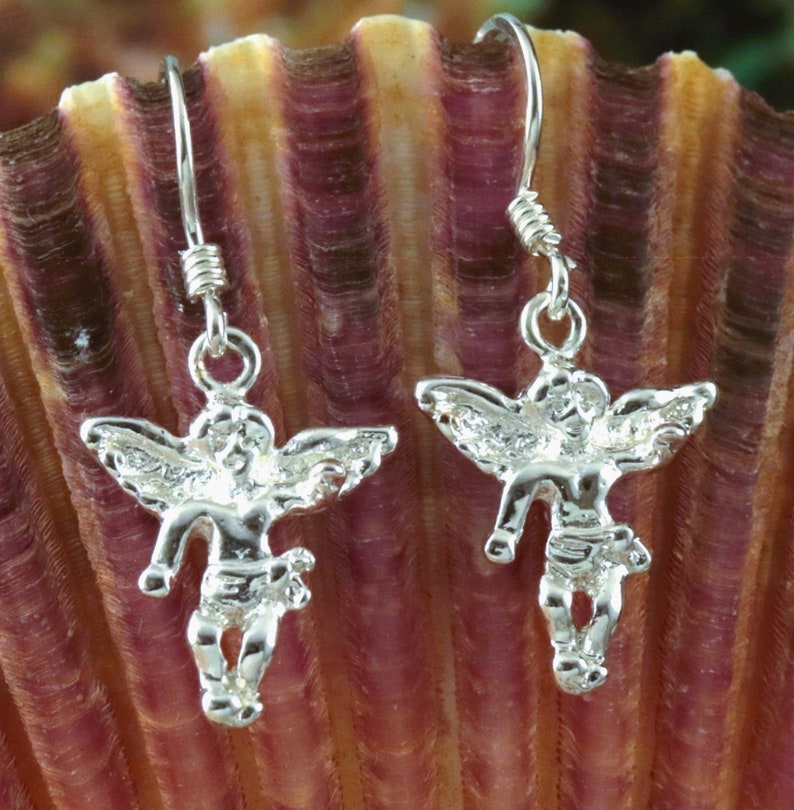 K&ouml;nnte beinhalten: Ein Paar silberne Ohrh&auml;nger mit einem Cherub-Design. Die Cherubim haben Fl&uuml;gel und stehen mit ausgestreckten Armen.