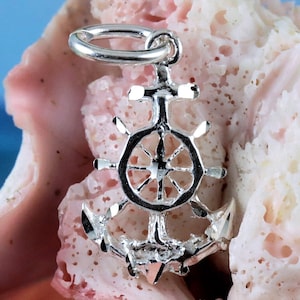 Könnte beinhalten: Silberner Anhänger mit einer detaillierten Anker mit einem Rad an der Oberseite. Der Anhänger ist im nautischen Stil gestaltet.