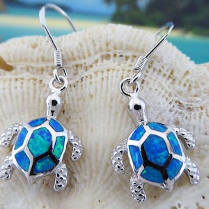 May include: Sterling silver earrings featuring a blue opal turtle charm. The turtle is detailed with a textured shell and has a silver hook closure.