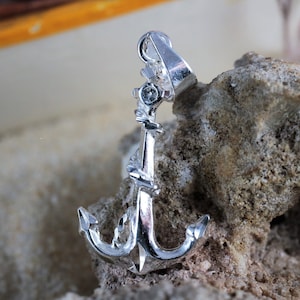 Könnte beinhalten: Ein silberner Anker-Anhänger mit einem kleinen, klaren Strassstein. Der Anker ist mit einem Seil verziert und hat oben eine Schlaufe zum Anbringen an einer Kette.