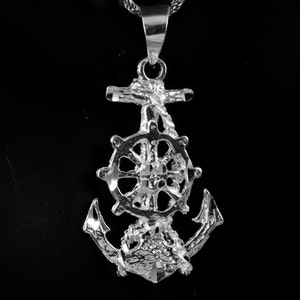 Könnte beinhalten: Silberner Anker-Anhänger mit einem detaillierten Schiffsrad-Design. Der Anker ist ein beliebtes nautisches Symbol.