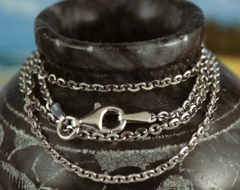 Puede incluir: Un collar de cadena de plata con un cierre de langosta. La cadena está sobre una superficie gris oscuro.