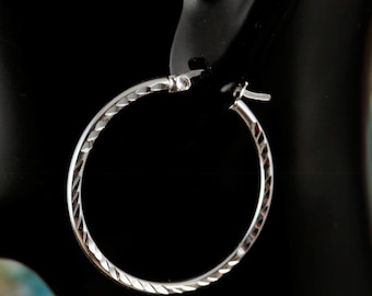 May include: A single silver hoop earring with a textured, diamond-cut pattern. The earring is displayed against a black background, showcasing its reflective surface and design. The hoop is a classic jewelry piece.