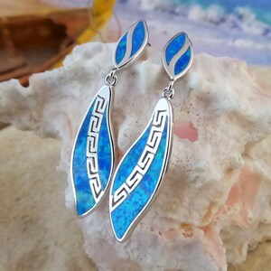 Puede incluir: Un par de pendientes colgantes de plata con piedras de ópalo azul y un diseño de llave griega.