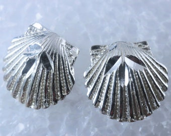 Puede incluir: Un par de pendientes de plata con forma de concha de vieira. Los pendientes están detallados con una superficie texturizada y un diseño en relieve.