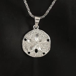 May include: A silver necklace with a detailed sand dollar pendant. The pendant is round and has a five-pointed star design in the center.