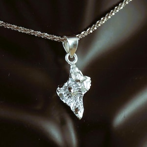 May include: A silver pendant necklace with a textured, geometric design. The pendant is shaped like a star or a diamond.
