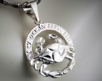 May include: A silver pendant necklace featuring a crab design within a circular frame. The frame is inscribed with "I LOVE OCEAN CITY, MD". The pendant hangs from a twisted silver chain, showcasing a detailed crab sculpture.