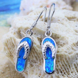 May include: A pair of silver dangle earrings featuring blue opal flip-flop charms. The earrings have a simple, elegant design and are perfect for summer.