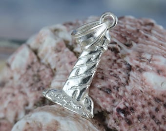 May include: Silver charm in the shape of a lighthouse with a striped design. The charm is sitting on a pink and white seashell.