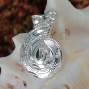 May include: A silver pendant in the shape of a spiral, with a detailed, textured design. The pendant has a loop at the top for attaching to a chain.