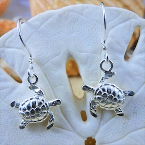 May include: Sterling silver dangle earrings featuring a detailed turtle design. The earrings are silver and have a polished finish.