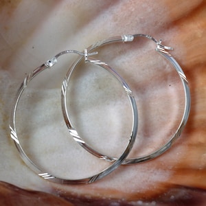 Puede incluir: Un par de pendientes de aro de plata con un diseño texturizado. Los pendientes son simples y elegantes.