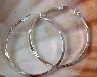 May include: A pair of silver hoop earrings with a textured design. The earrings are simple and elegant.